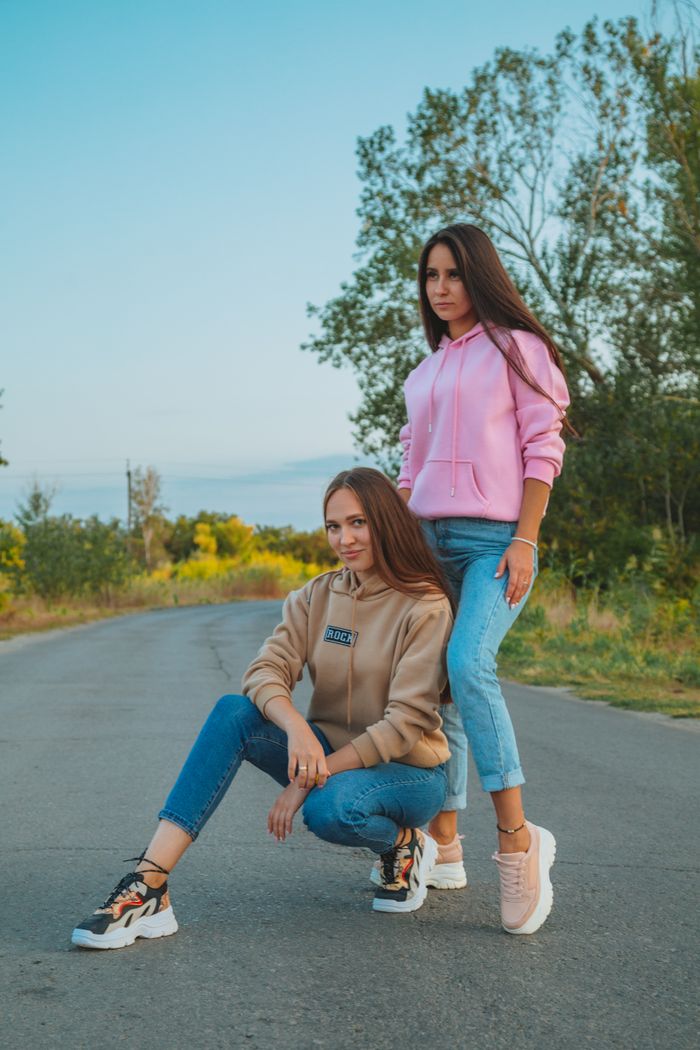 Full body of young female in casual outfits standing on asphalt roadway and looking away