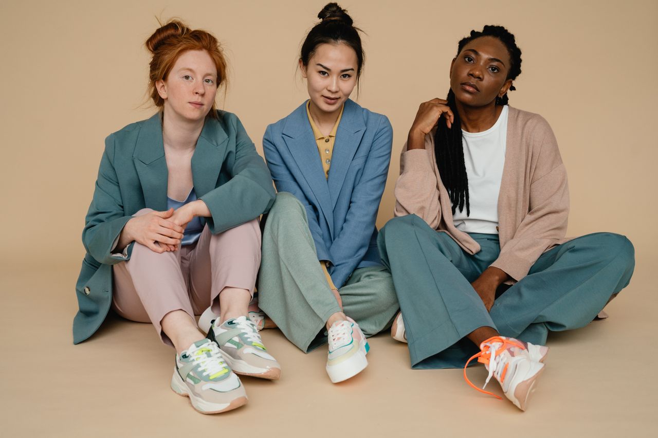 Three diverse women sitting in colorful suits against a beige backdrop, showcasing fashion and diversity.